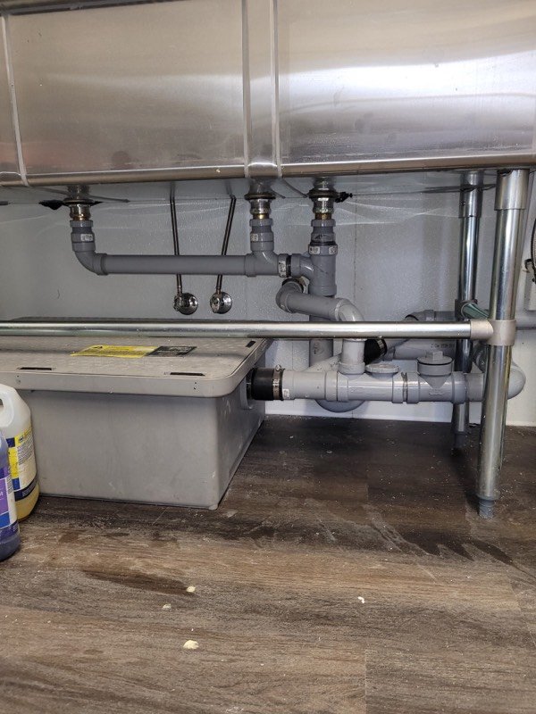 PVC drain piping and a grease interceptor beneath a stainless steel commercial kitchen sink