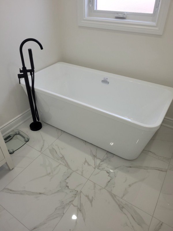 Freestanding soaker tub with a black floor-mounted filler installed in a renovated bathroom