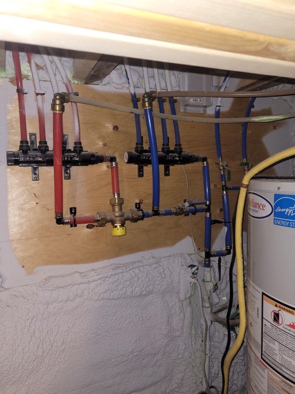 PEX manifold with red and blue water supply lines feeding a hot water tank in a Brantford basement