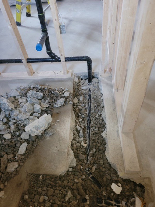 Open trench cut through a basement floor slab with new ABS drain pipe laid in gravel