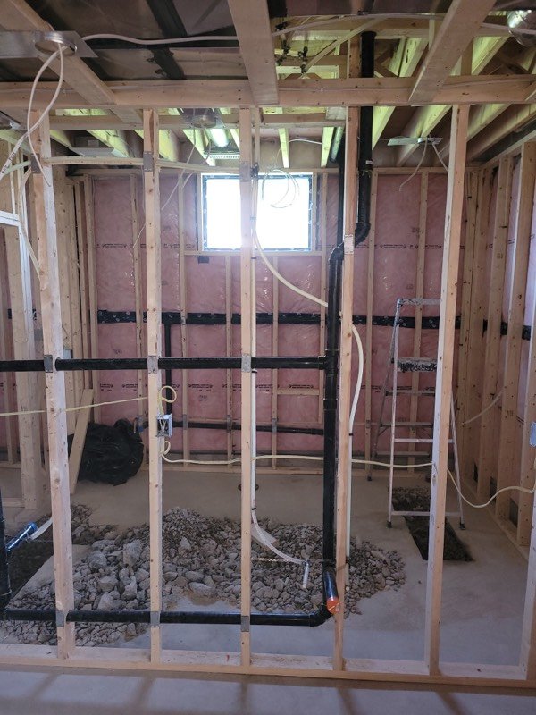Basement bathroom rough-in with framed walls, insulation and black ABS drain lines set into gravel