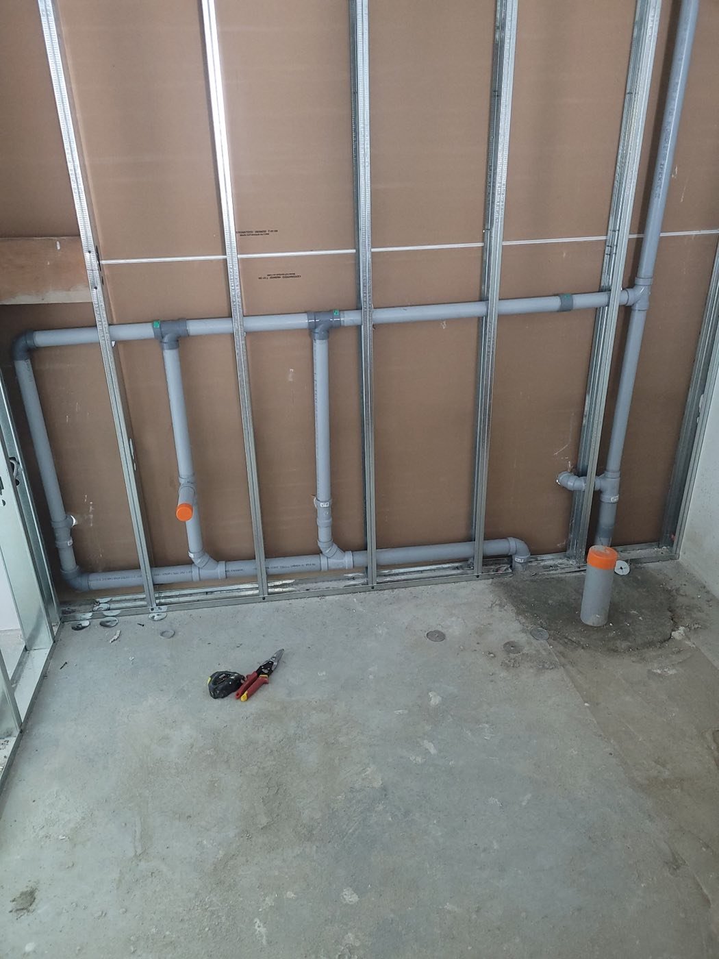 PVC drain lines roughed in across steel stud framing in a commercial washroom