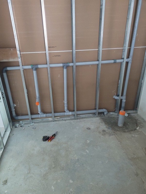 PVC drain lines roughed in across steel stud framing in a commercial washroom