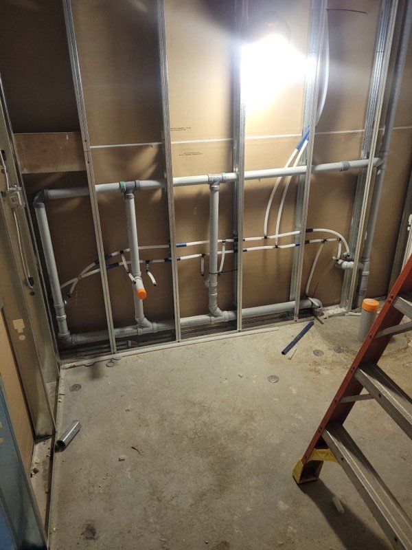 Water supply and PVC drain lines roughed in through steel stud framing before drywall