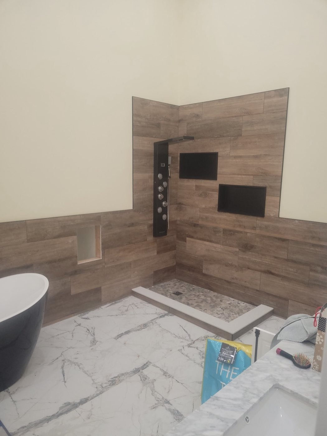 Finished bathroom with a wood-look tile feature wall, black shower panel and freestanding tub