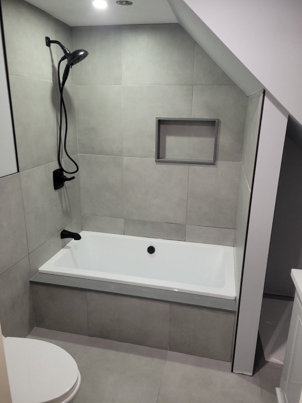 Finished bathroom with a drop-in soaker tub, large-format grey tile and a tiled niche, installed by Baptiste Plumbing Service