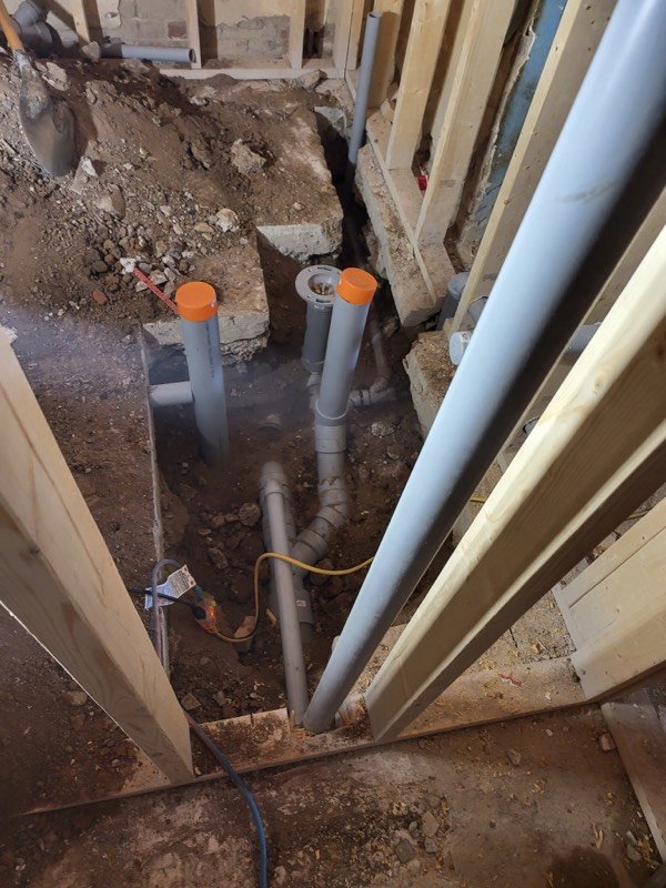 PVC drain stacks standing in an open excavation between framed basement walls