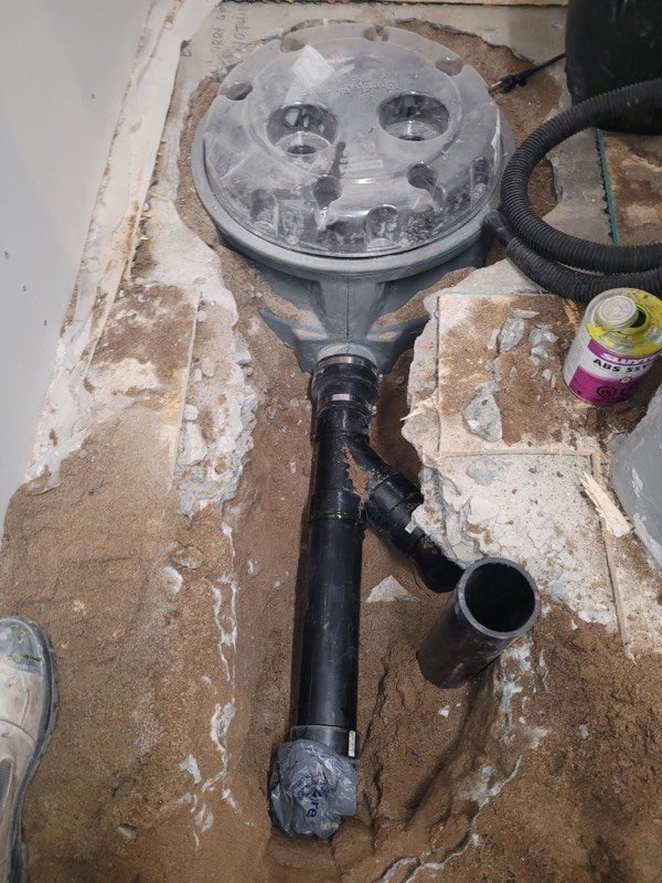 New floor drain and clean-out set into a broken concrete floor before the slab is restored