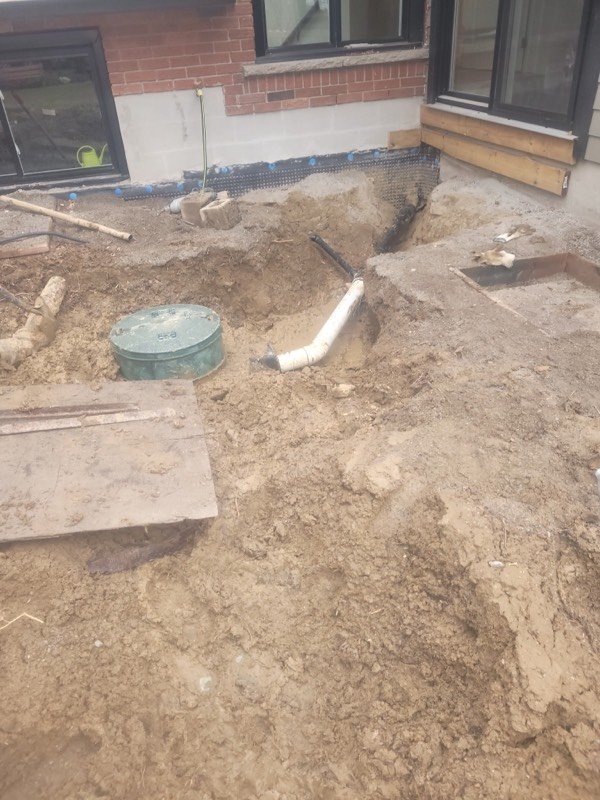 Excavated trench in a back yard exposing the water service line and a clean-out beside the house