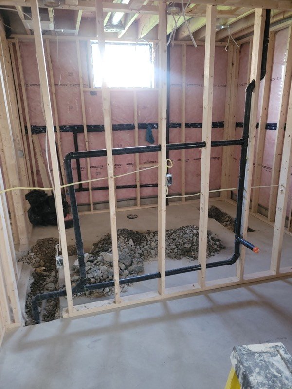 Bathroom rough-in with black ABS drain lines run through stud framing and set into gravel