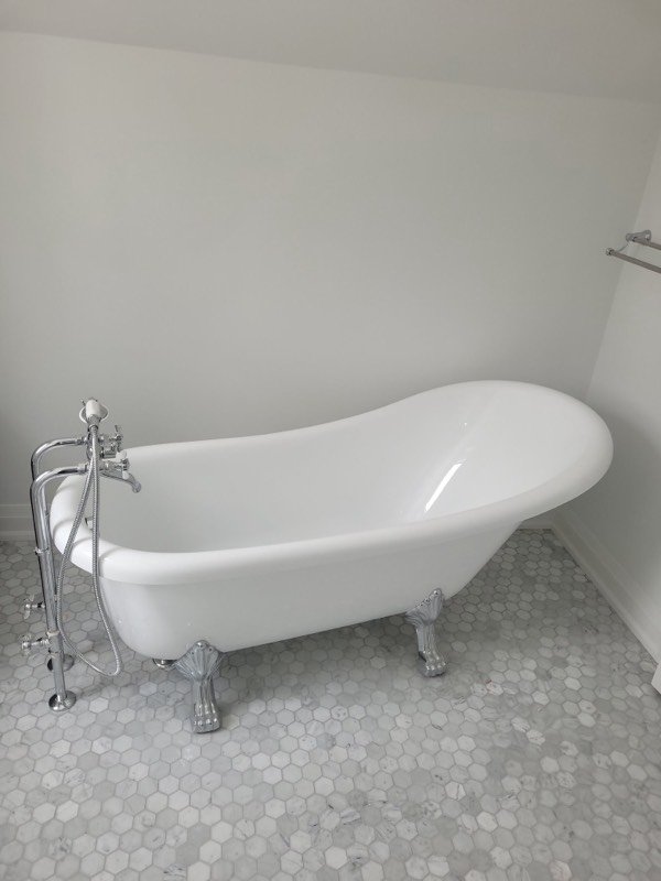 Freestanding clawfoot slipper tub with a chrome floor-mounted filler on a hexagonal marble tile floor