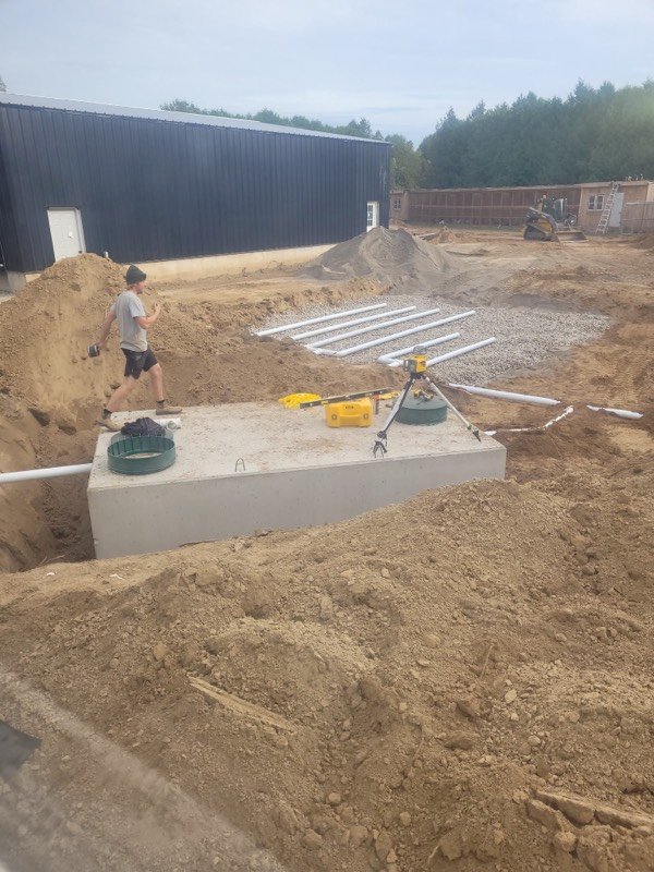 Site excavation showing an underground concrete tank with access risers before backfilling
