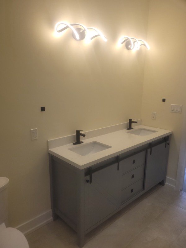 Grey double vanity with a white quartz counter, black faucets and sculptural wall lights