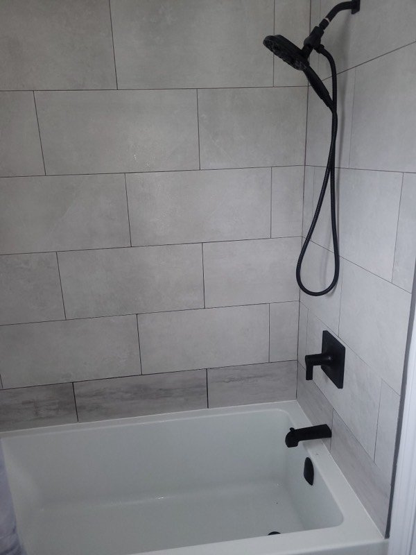 Finished bath and shower with large-format grey tile and matte black valve, spout and hand shower