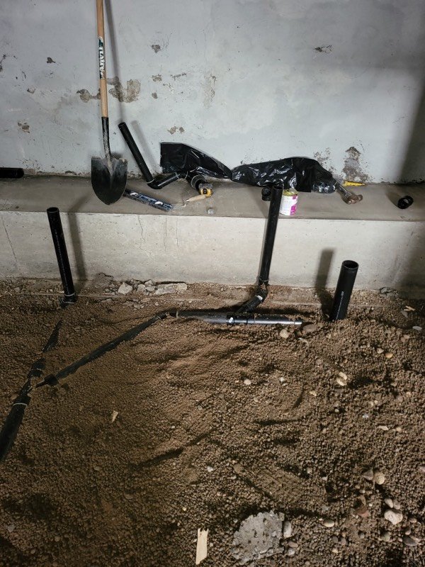 Black ABS drain stacks standing in excavated gravel below a basement slab