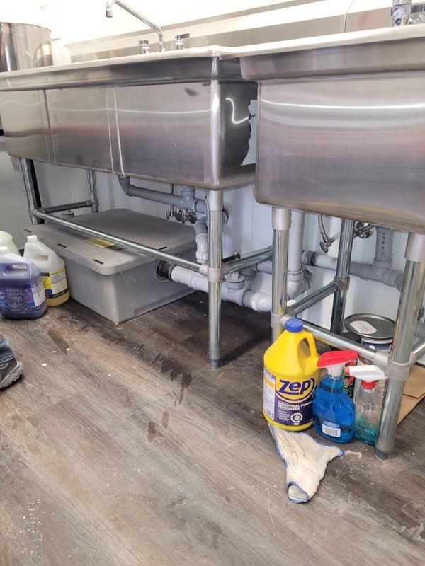 Drain piping and grease interceptor beneath a stainless steel commercial kitchen triple sink