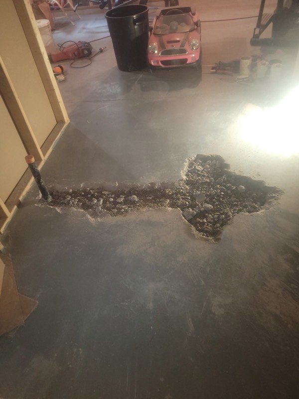 Concrete garage floor broken open along the run of a new underground drain line