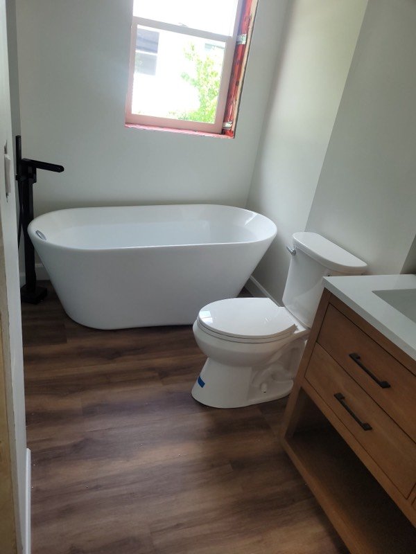 Finished bathroom with a freestanding tub, new toilet and wood vanity on wood-look flooring
