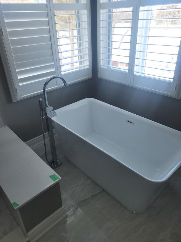 Freestanding soaker tub with a chrome floor-mounted filler set below shuttered windows