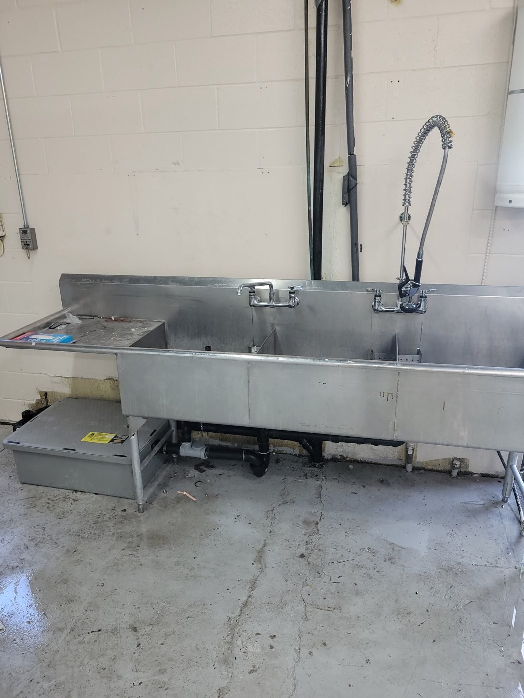 Stainless steel commercial triple sink with pre-rinse sprayer and a grease interceptor beneath