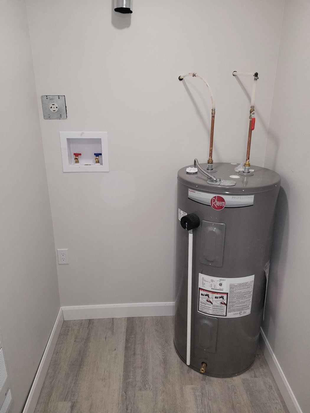 Newly installed electric hot water tank beside a recessed laundry box in a finished utility room