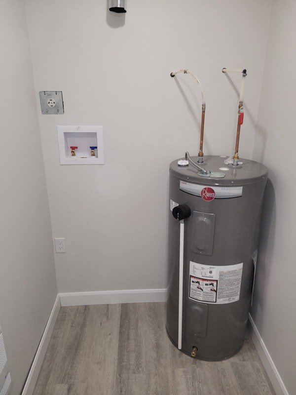Newly installed electric hot water tank beside a recessed laundry box in a finished utility room