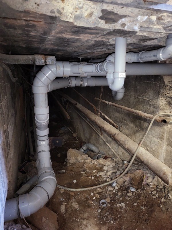 PVC drain and vent piping run through a low crawl space beneath a house