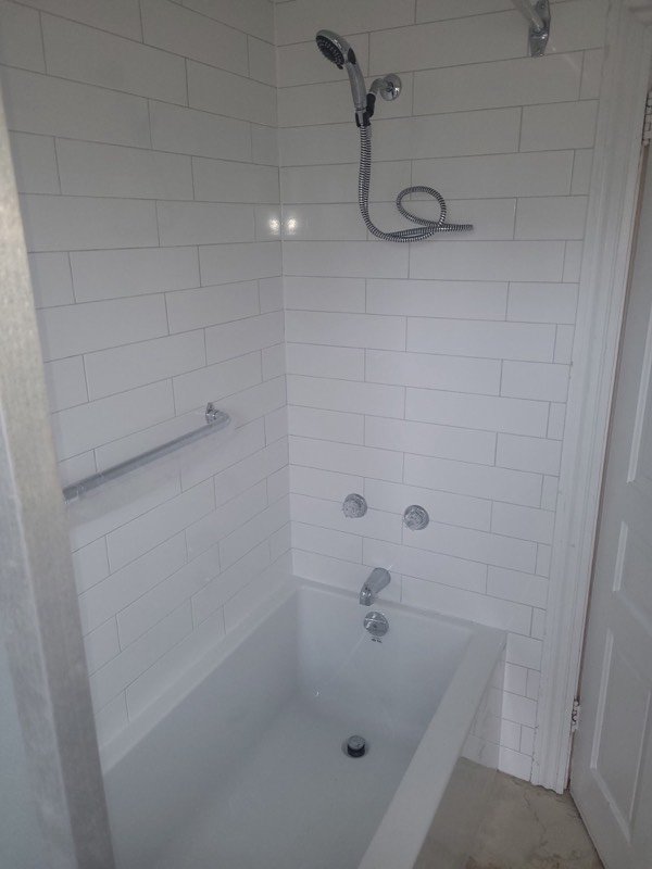Finished tub and shower surround in white subway tile with chrome valve, spout and hand shower