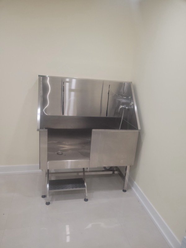 Stainless steel walk-in wash tub with a hand shower installed in a tiled commercial room