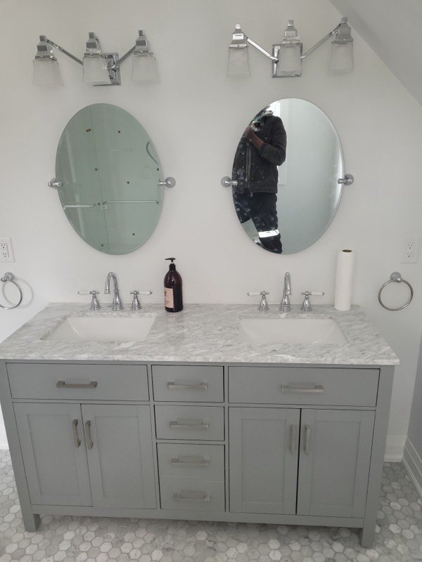 Finished double vanity with a marble top, oval mirrors, chrome faucets and wall sconces
